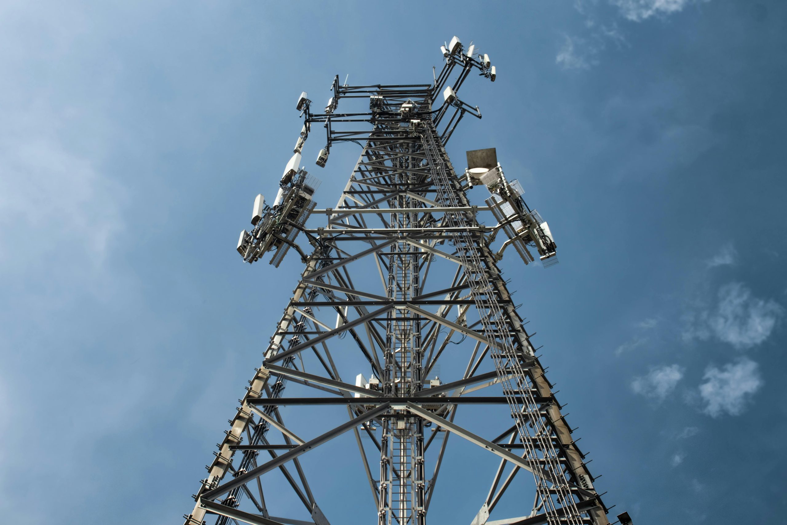 A low-angle shot of a tall metal communications tower with multiple antennas against a clear blue sky.